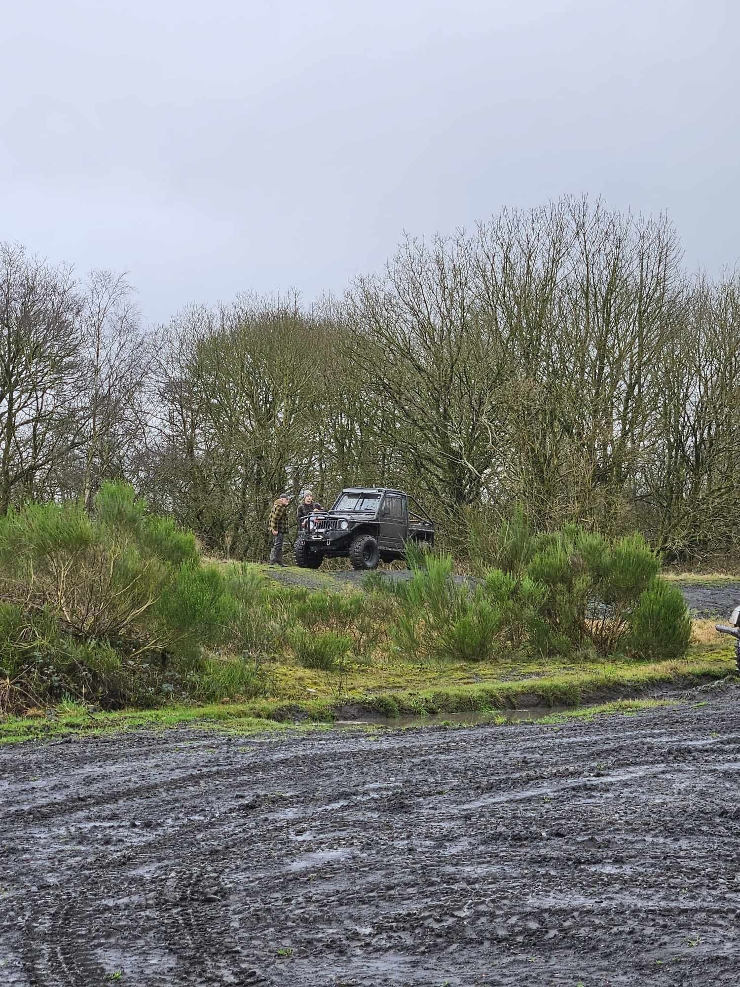 Off-road vehicle on a grassy slope beside a muddy track
