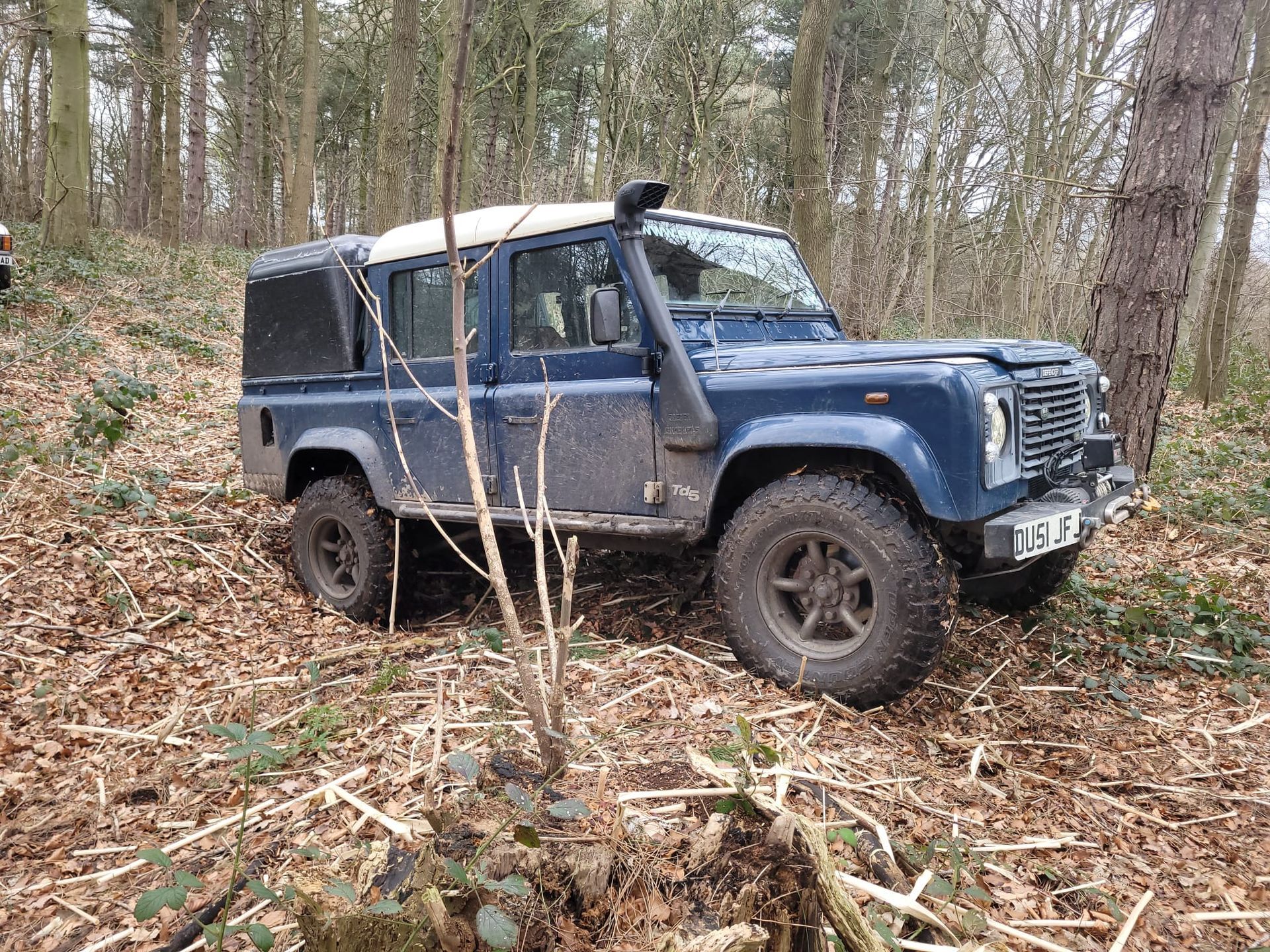 Blue Defender parked on a leaf-covered woodland trail