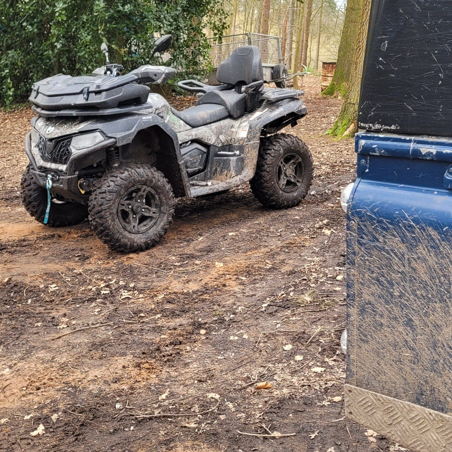Quad bike parked beside a blue Defender in woodland