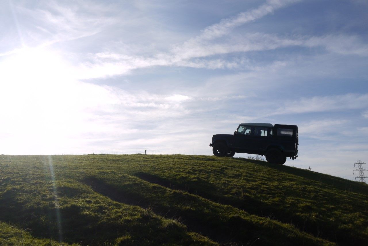 Land Rover Defender silhouetted on a ridge beneath a bright sky
